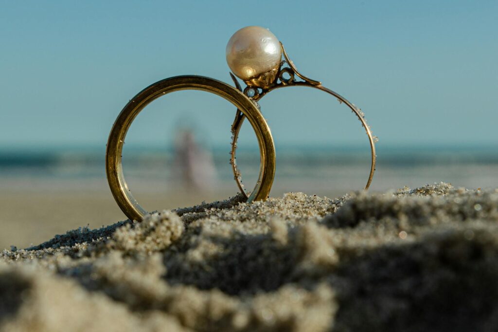 A close-up of wedding rings resting on sandy beach with waves in the background. — romantic beach wedding Las Vegas