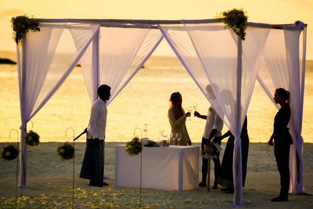 A couple enjoying their beach wedding reception with guests dining in the background. — beach wedding catering Las Vegas