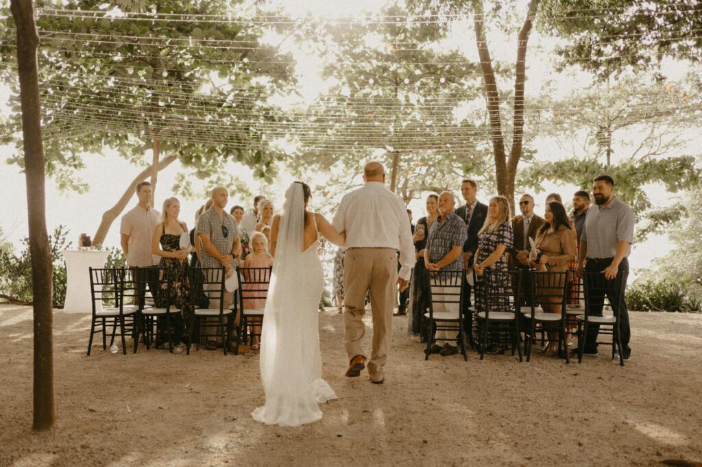 A couple exchanging vows on the beach during a summer sunset, with guests enjoying the warm weather. — best time beach w…
