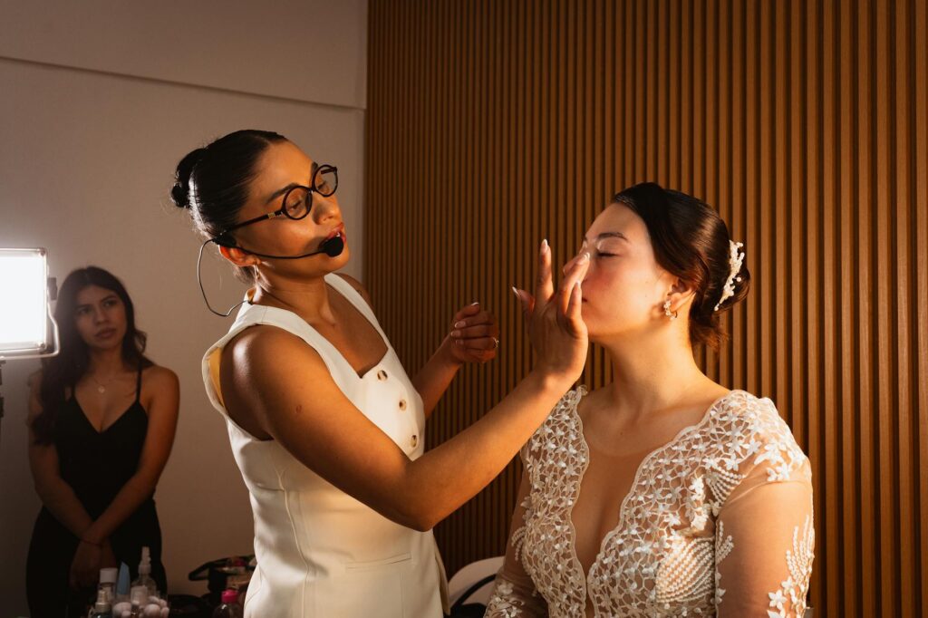 Bridesmaids assisting the bride with makeup on the beach. — beach wedding makeup Las Vegas
